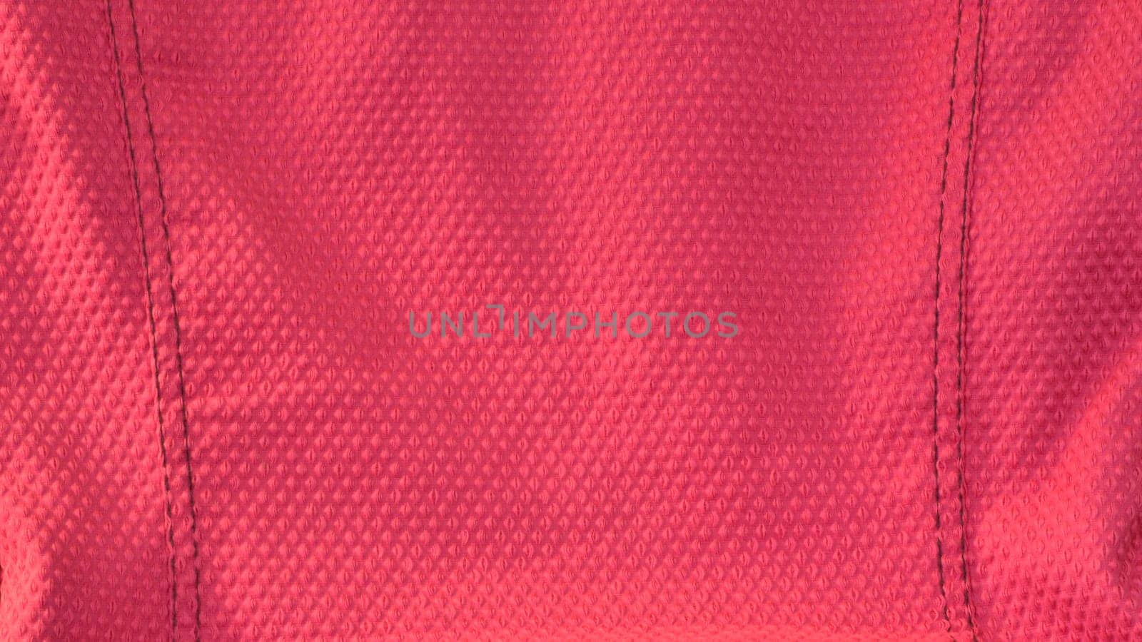 Vivid hot pink fabric background. Closeup of a textured pink fabric with black stitch detailing on both sides. Letterbox shape.