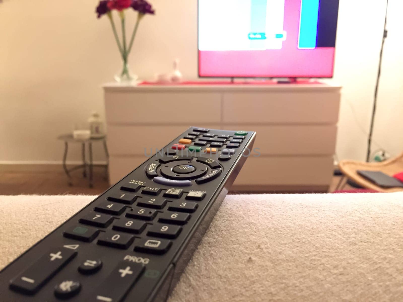 Close up of a remote controller with a television on background