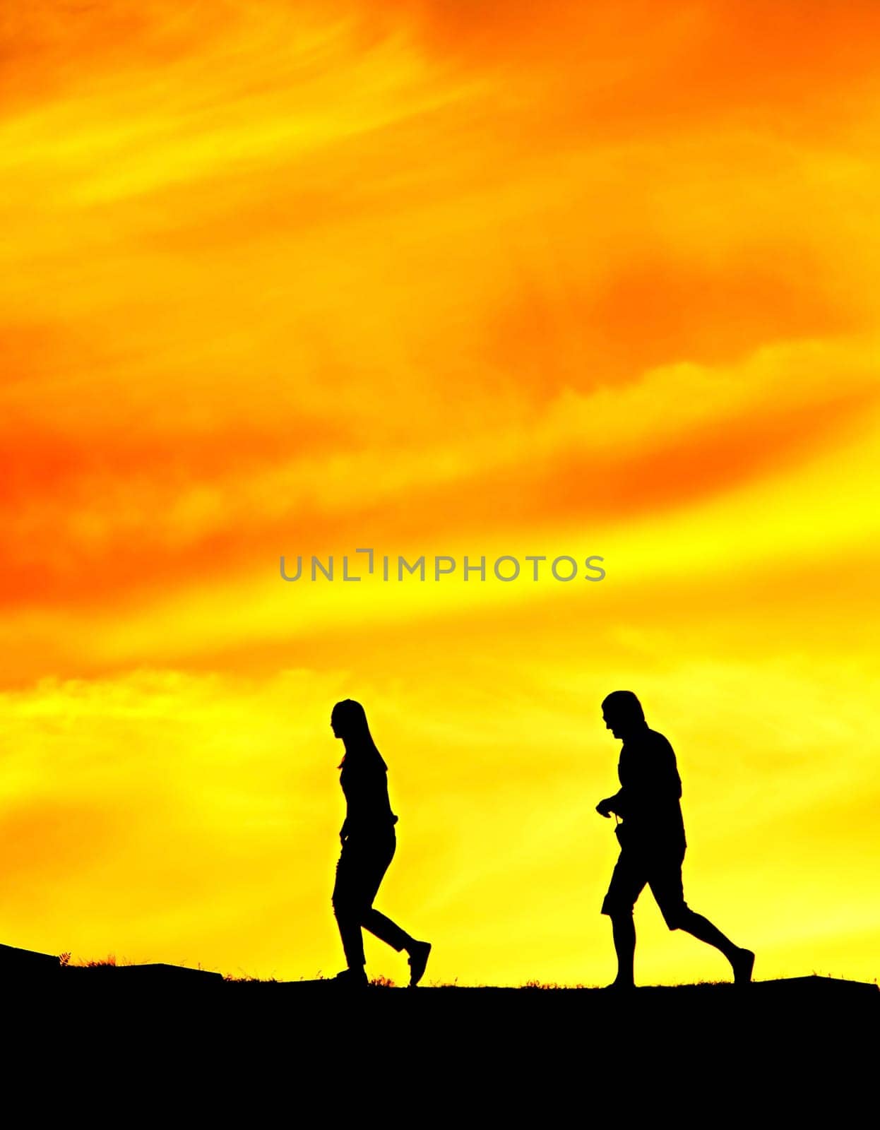 Woman and man walking one after another on a park at sunset