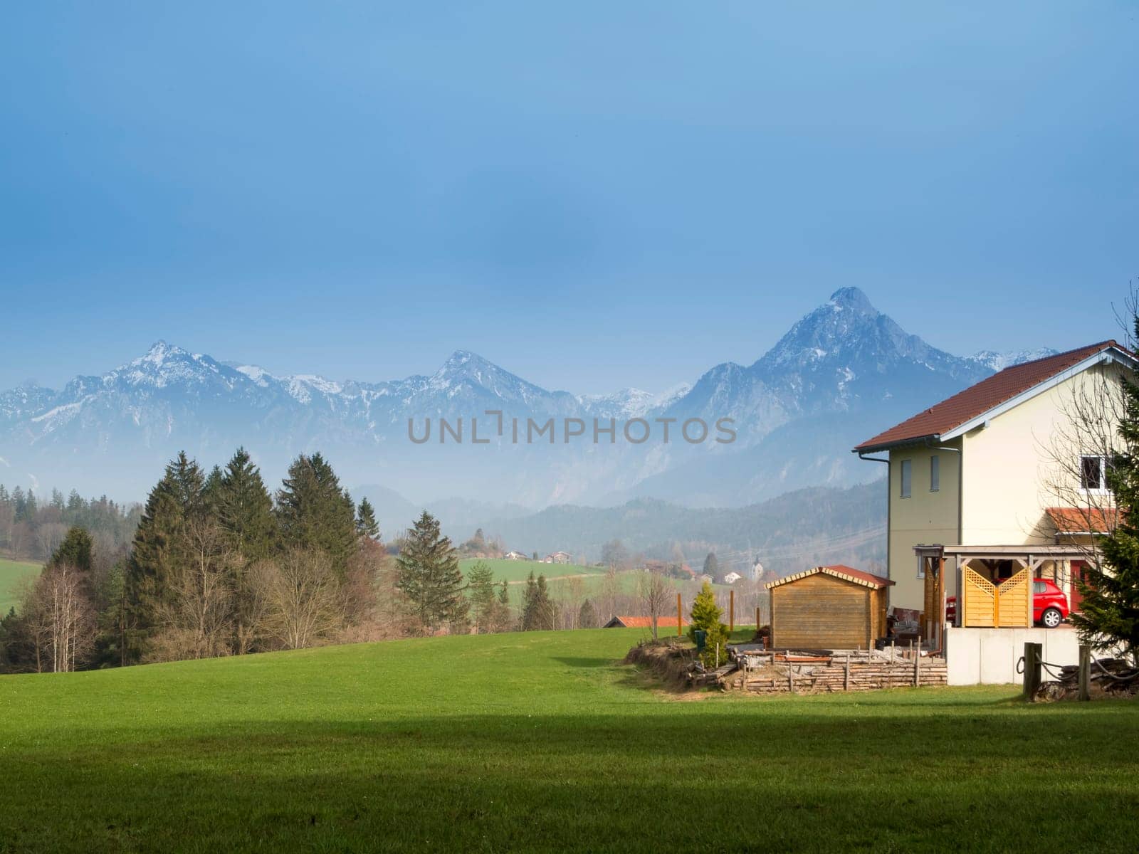 Allgäu landscape with house in the foreground,meadow and forest in the middle of the picture and alpine mountains in the background