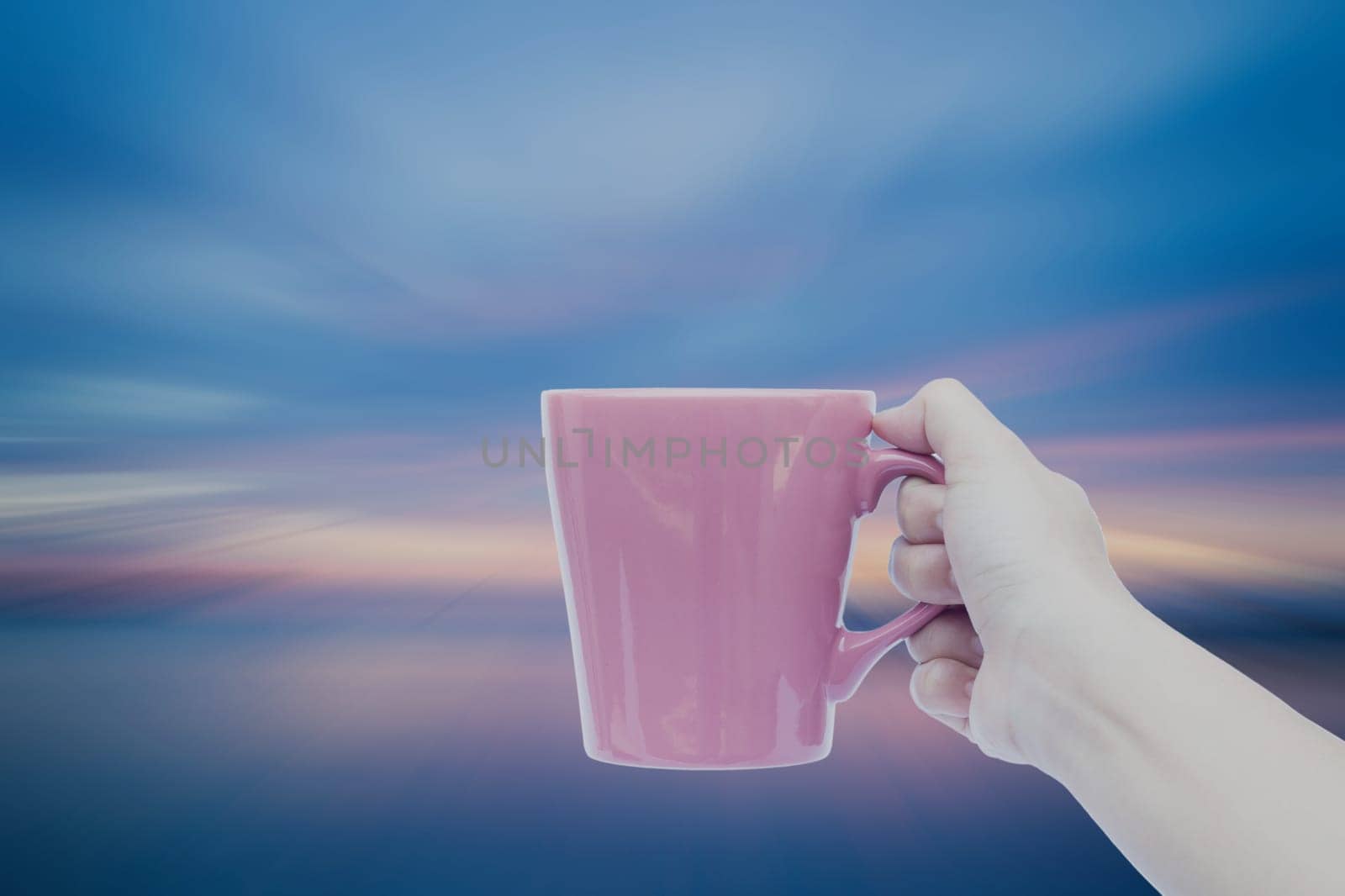 Woman hand holding coffee cup with sunset blur background, stock photo