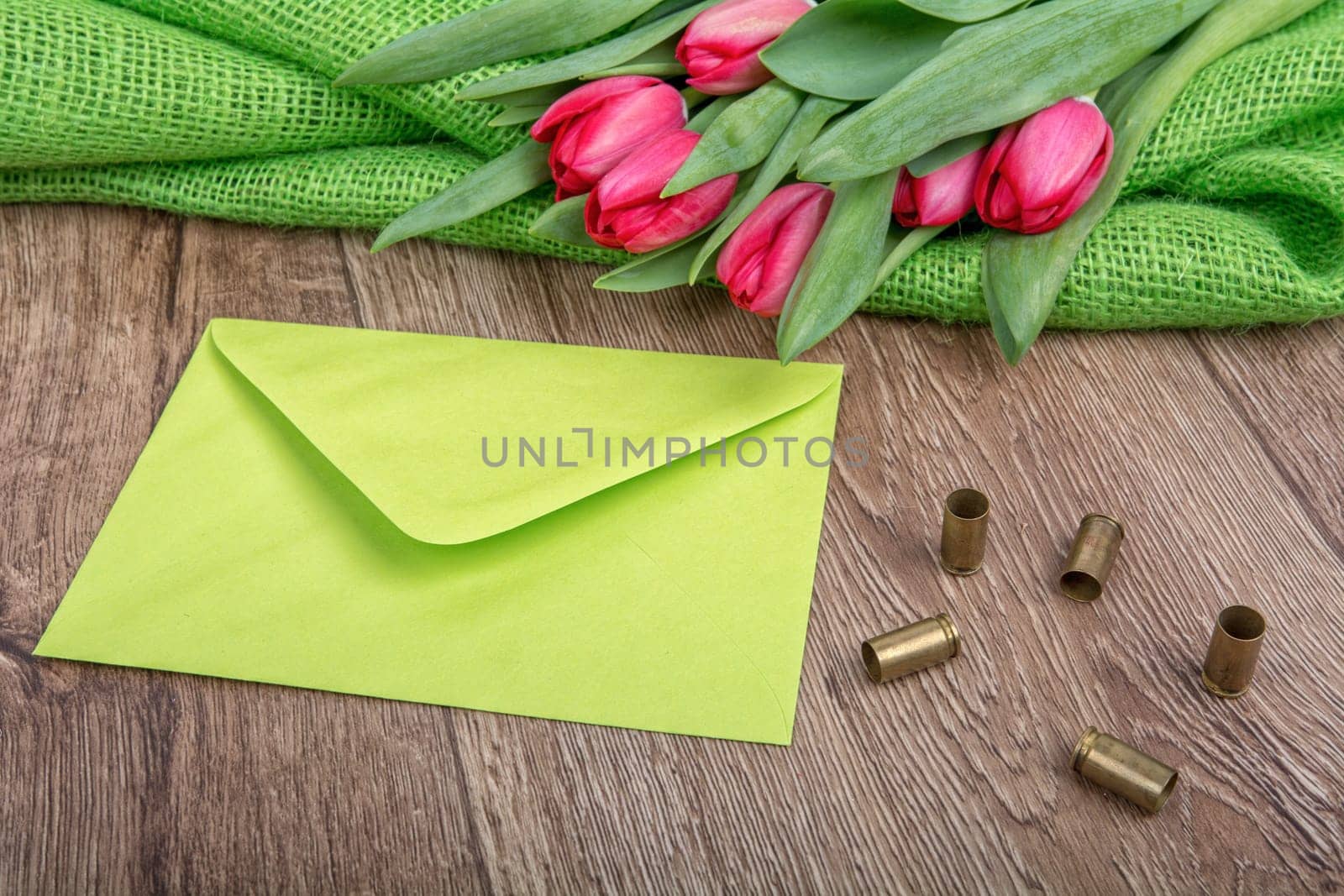 Green envelope, tulips and bullets on a wooden background