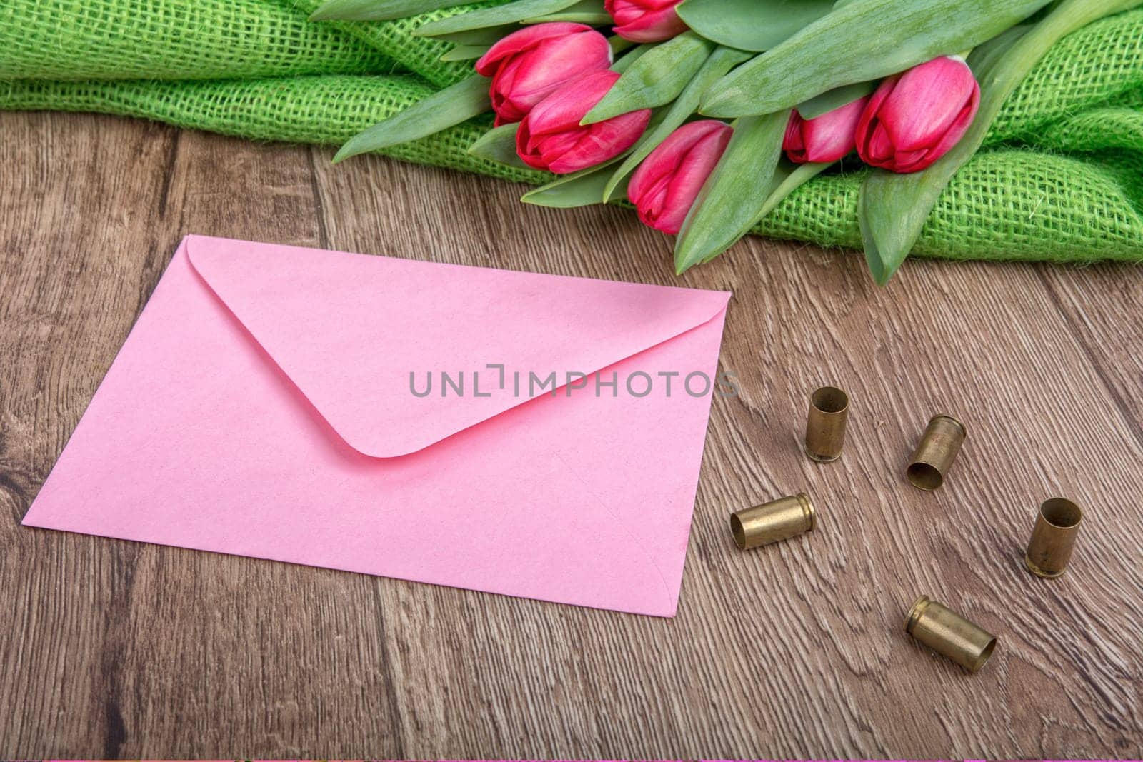 Pink envelope, tulips and bullets on a wooden background