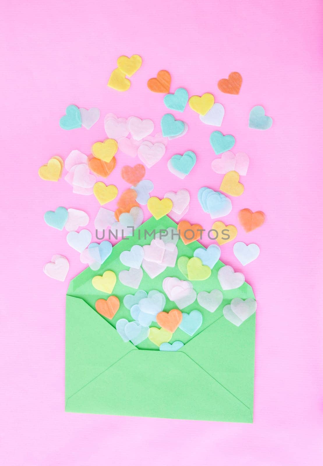 Colorful heart confetti from green envelope on pink