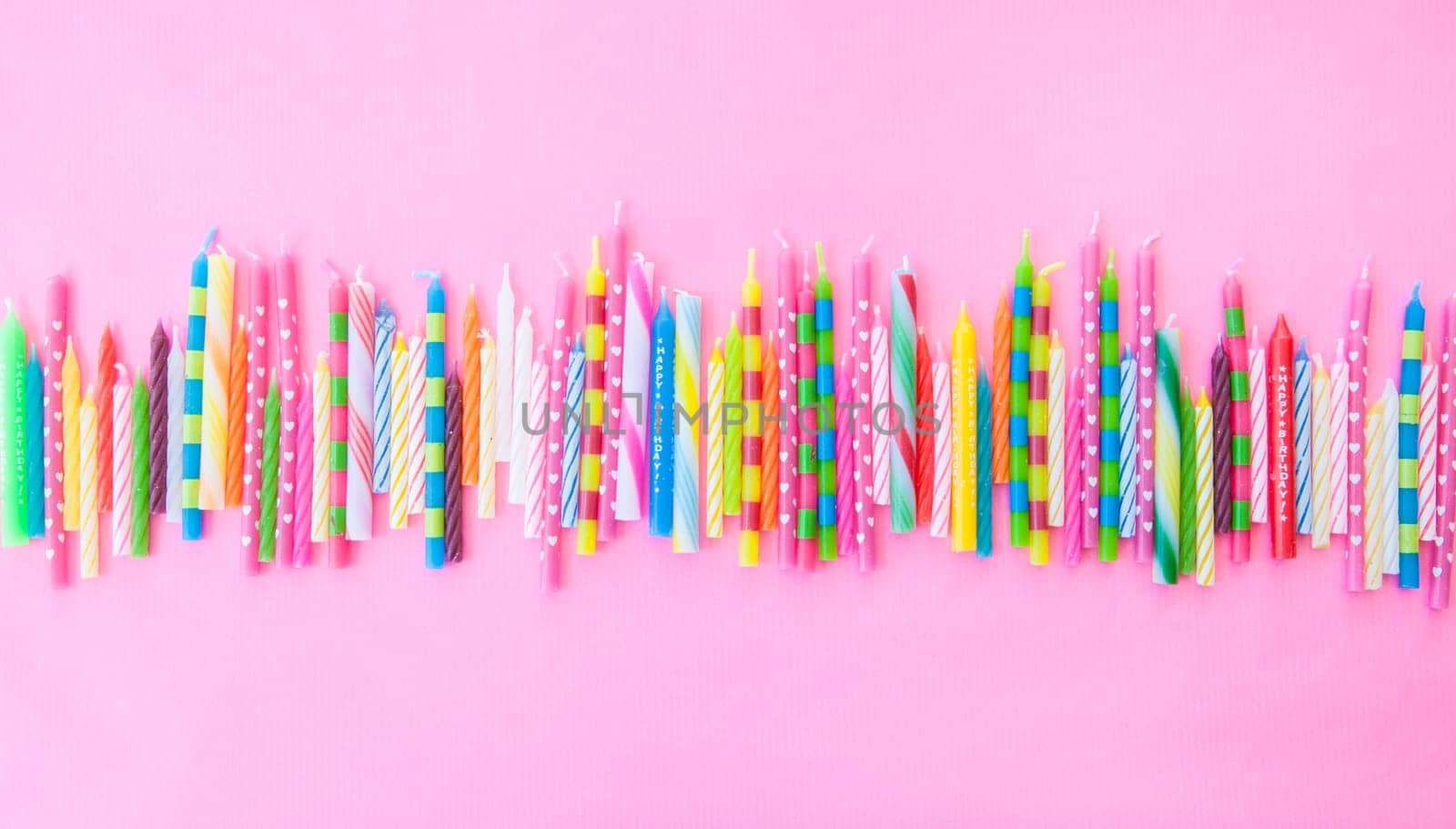 Various colorful birthday candles lined up on pink