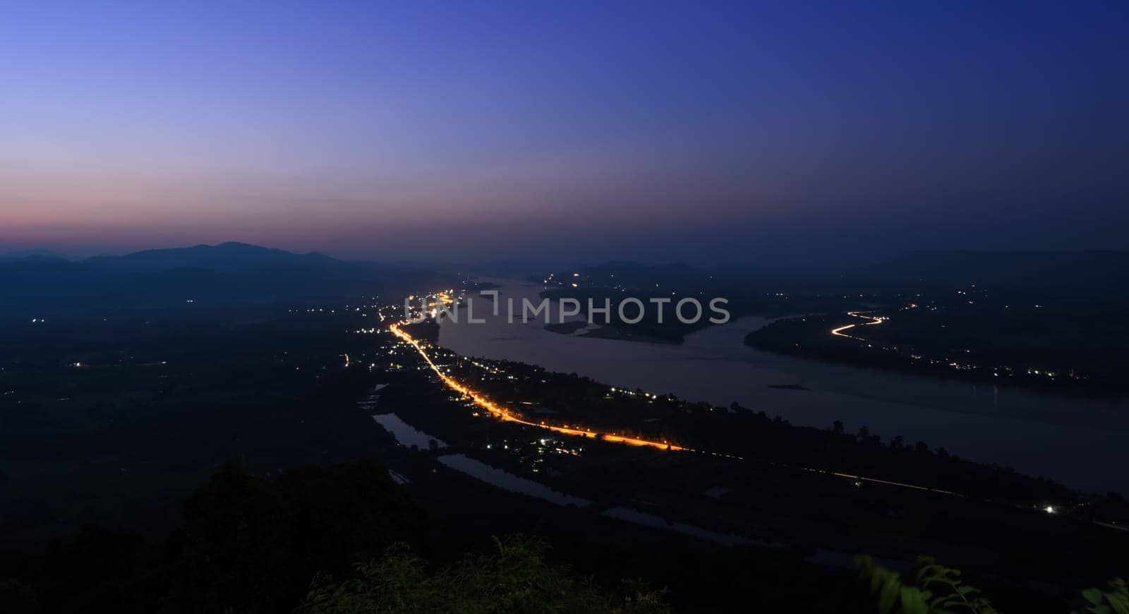 Aerial landscape view of Mekong river with mountain ranges at twilight in Nong Khai Province, Thailand. Long exposure shot with street light trails