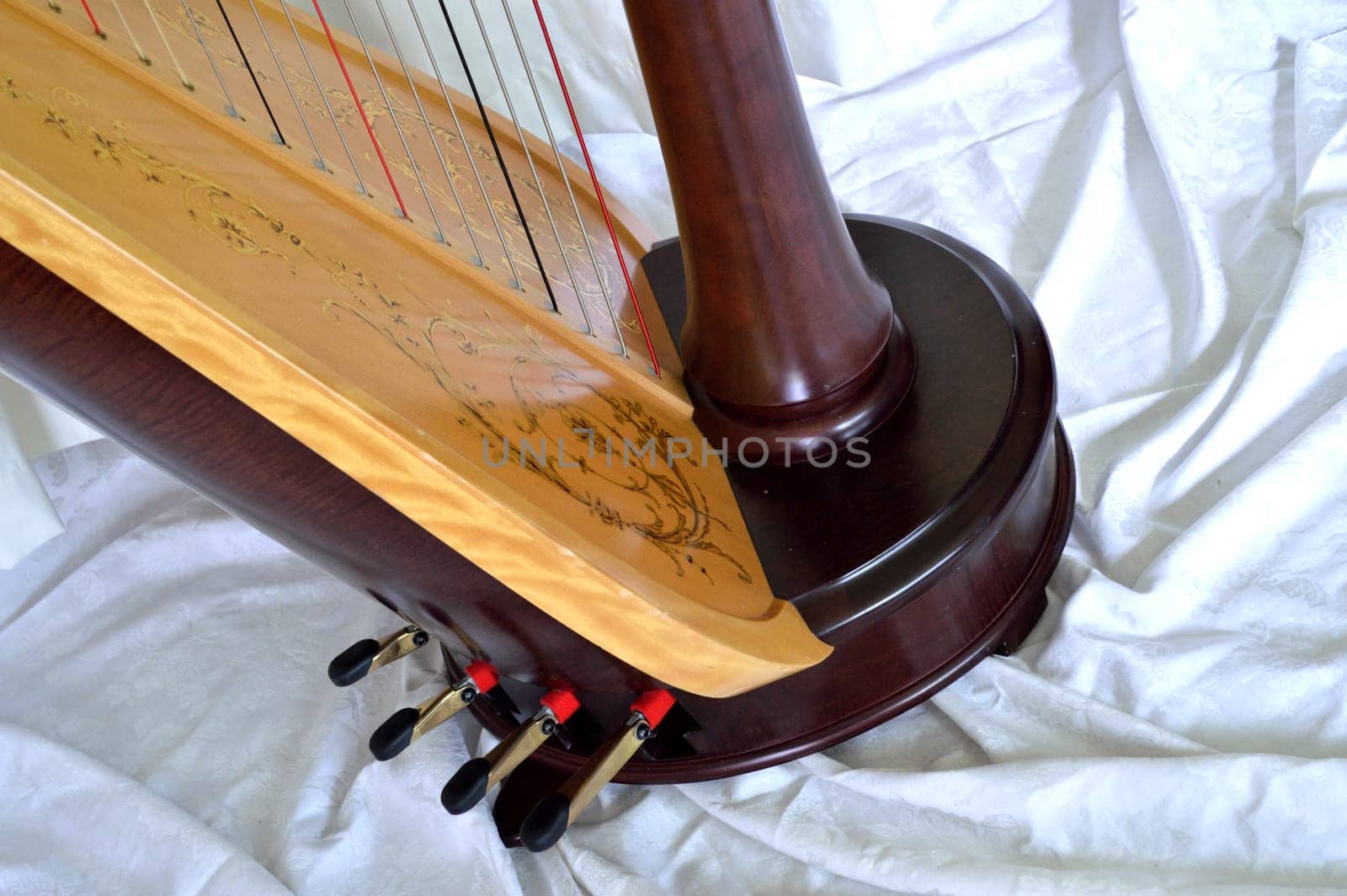 Closeup of the base of a dark wood, concert grand, pedal harp. Pedals and soundboard in detail.