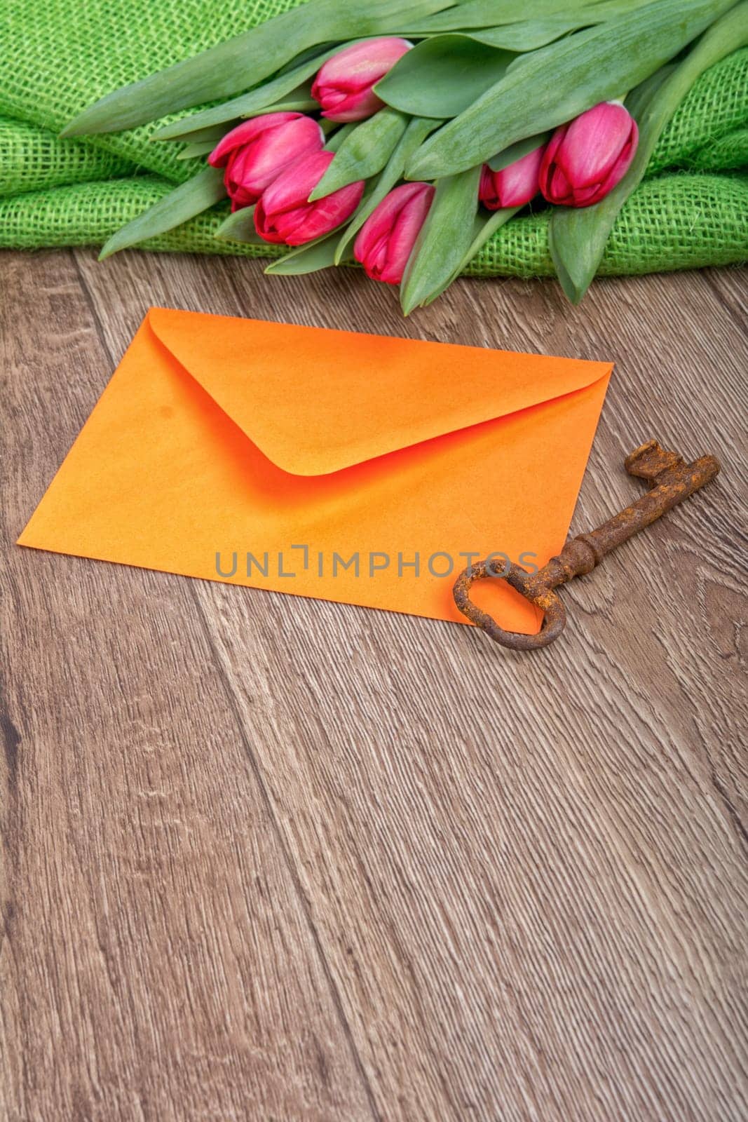 Envelope, rusty key and red tulip on a wooden background