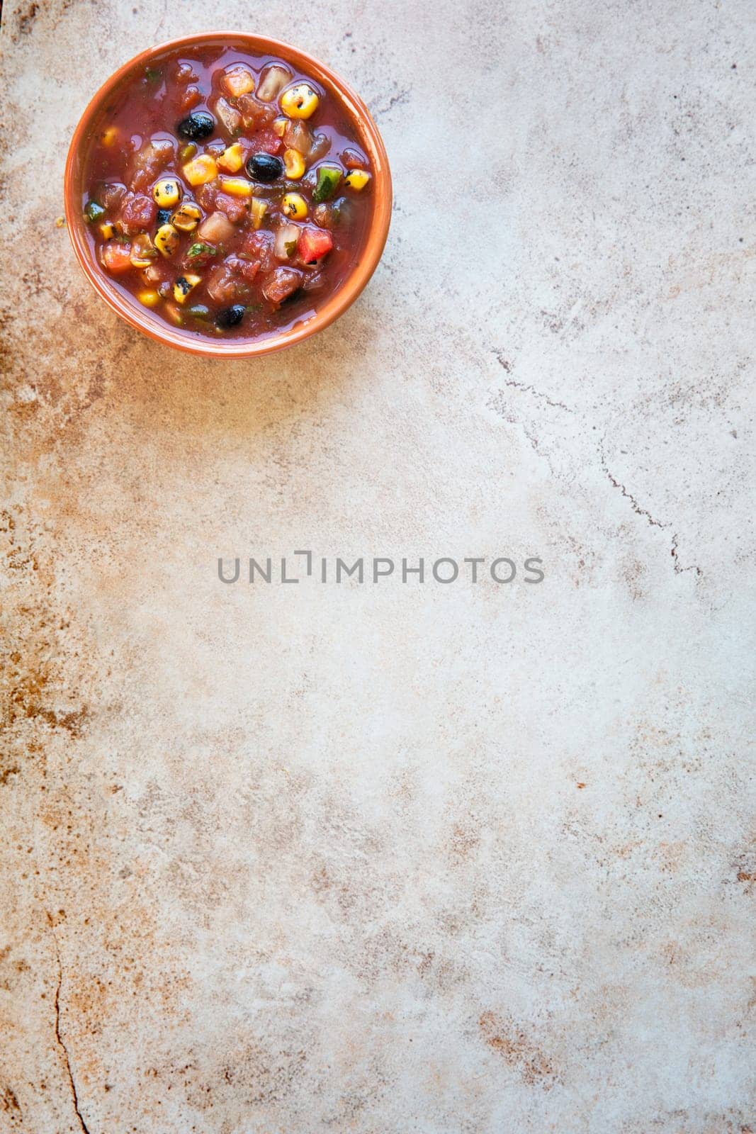 Bowl of fresh salsa on stone surface with copy space and viewed from above.