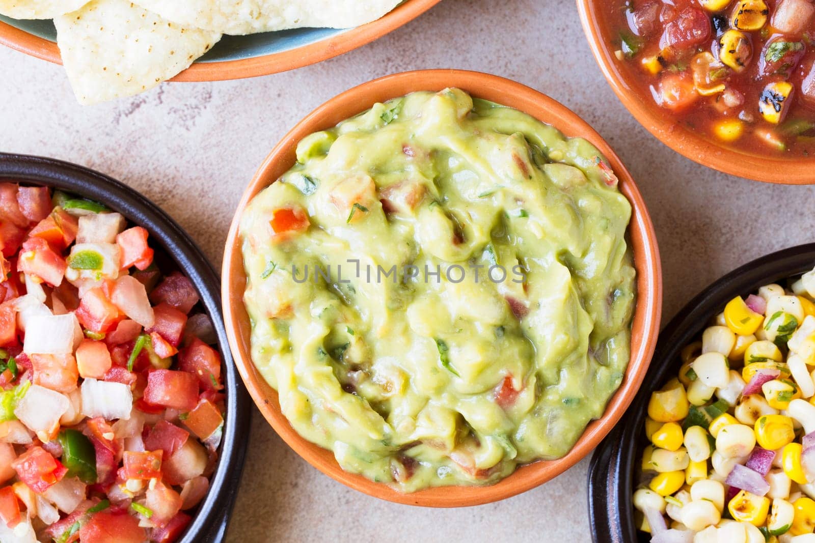 Close up of guacamole surrounded by pico de gallo and salsa, top down view