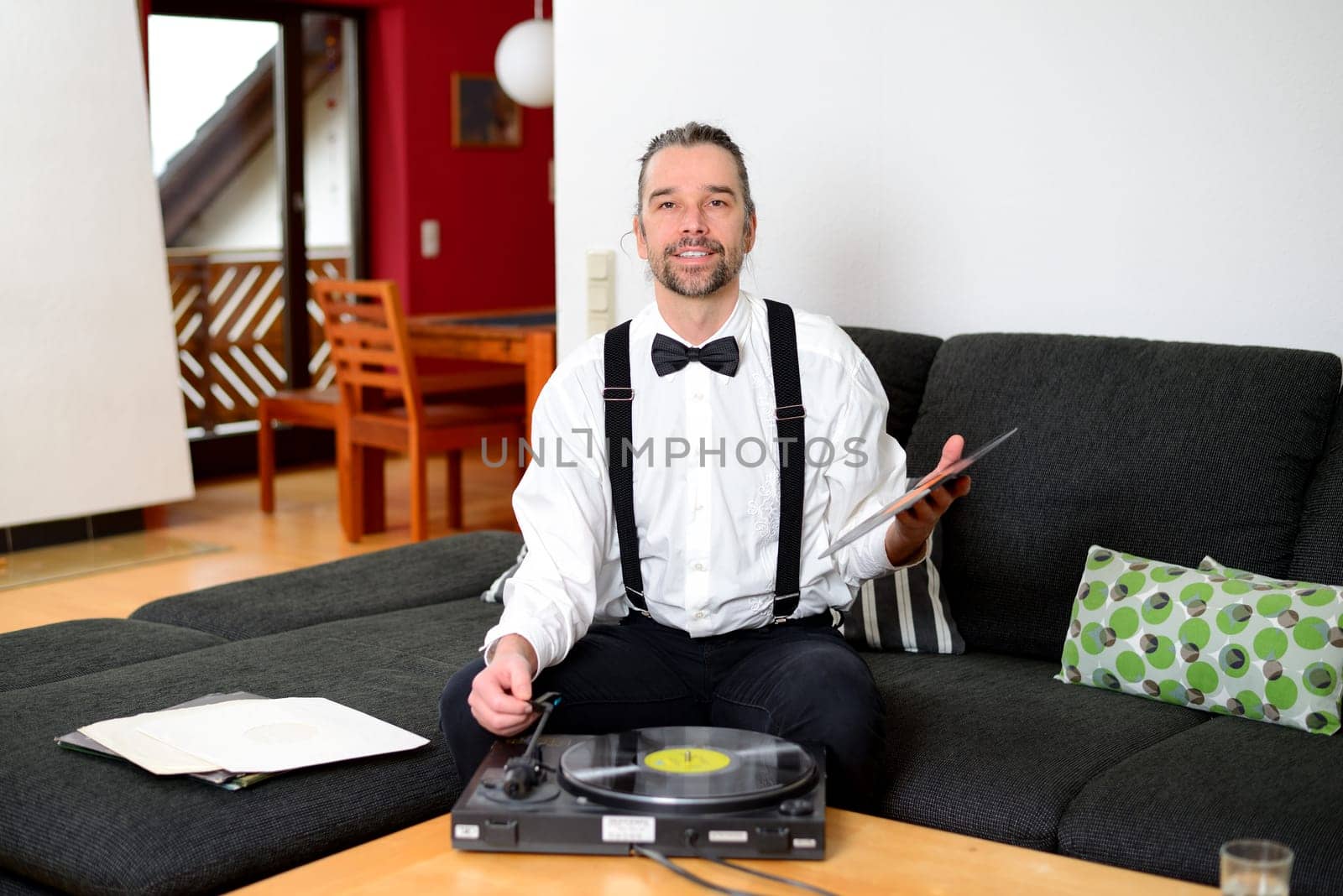 young man in white shirt with bow-tie with old records in his living room