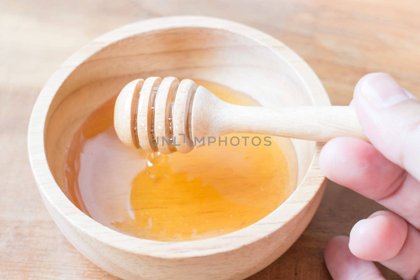 Hand on honey dipper from wooden cup, stock photo