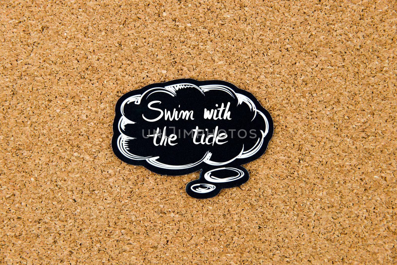 SWIM WITH THE TIDE written on black thinking bubble over cork board background, copy space available