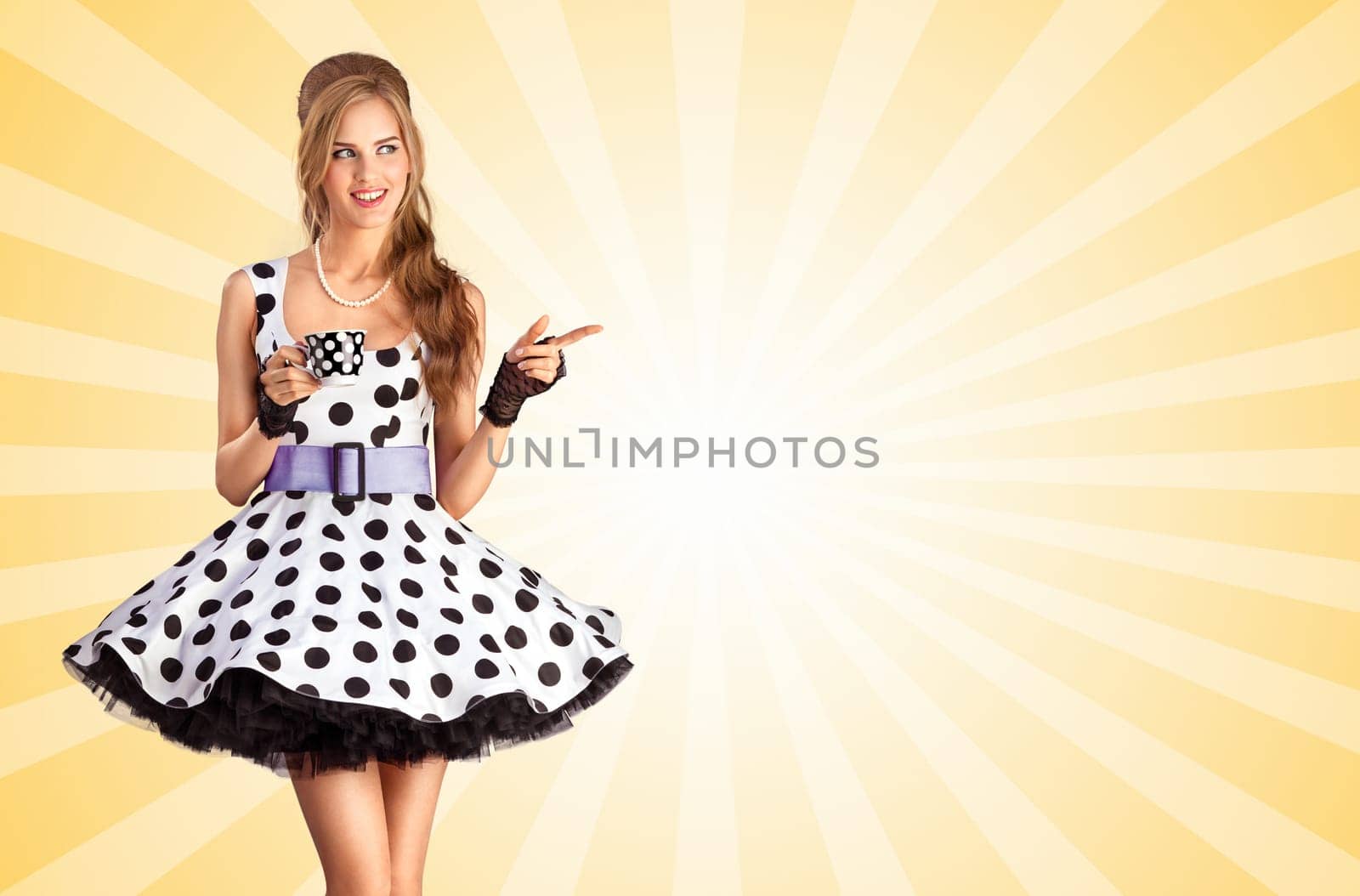 Creative vintage photo of a beautiful pin-up girl in a polka dot dress, holding a cup of tea and pointing aside on colorful abstract cartoon style background.