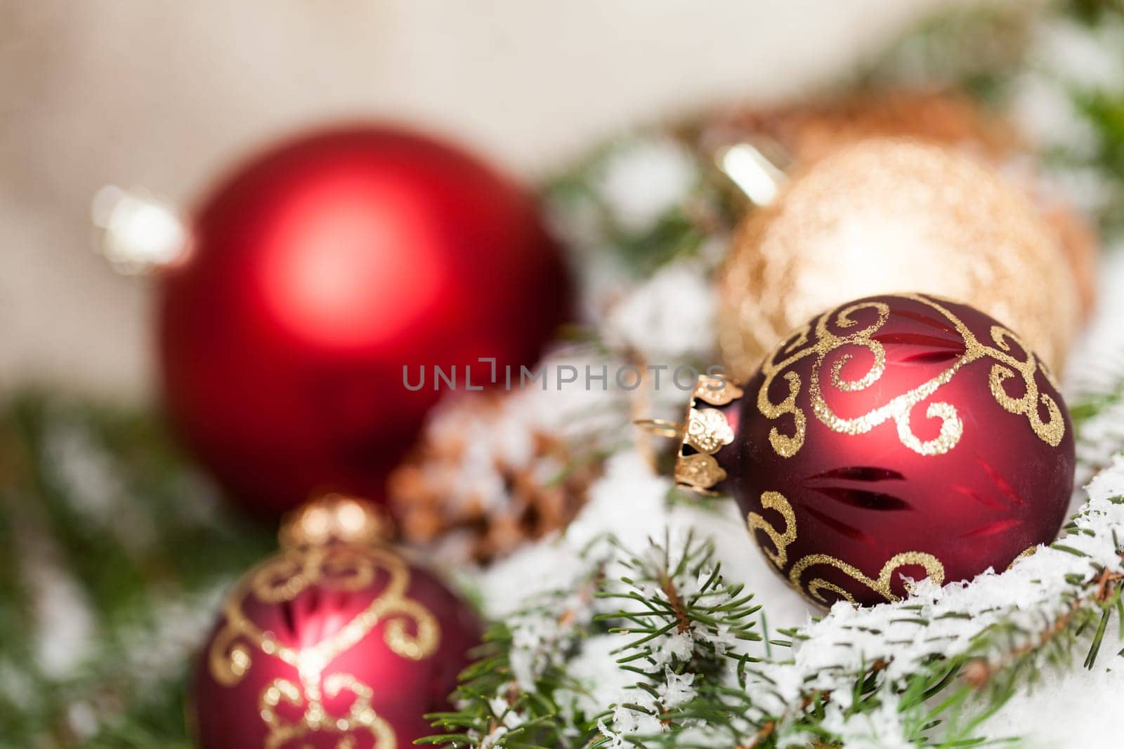 red Christmas baubles between cones and fir branches covered with snow as macro detail
