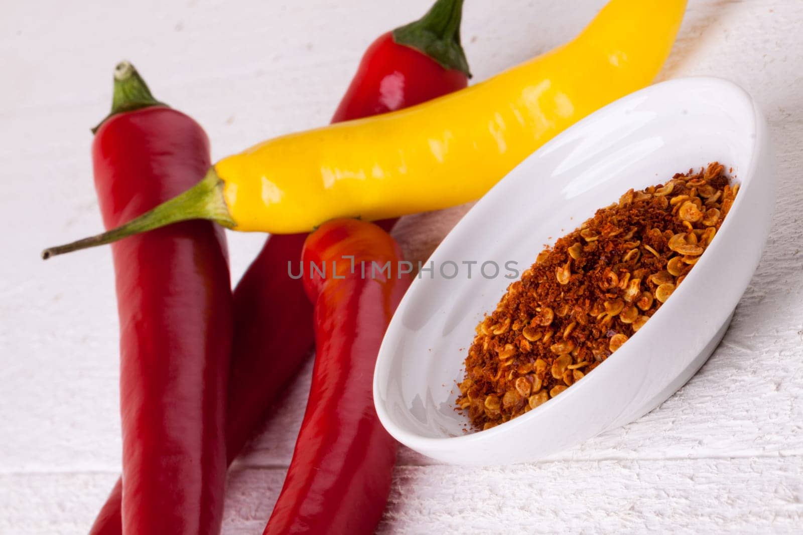 Fresh pepperoni and chilli with chili powder as a close-up on a white rustic wooden board