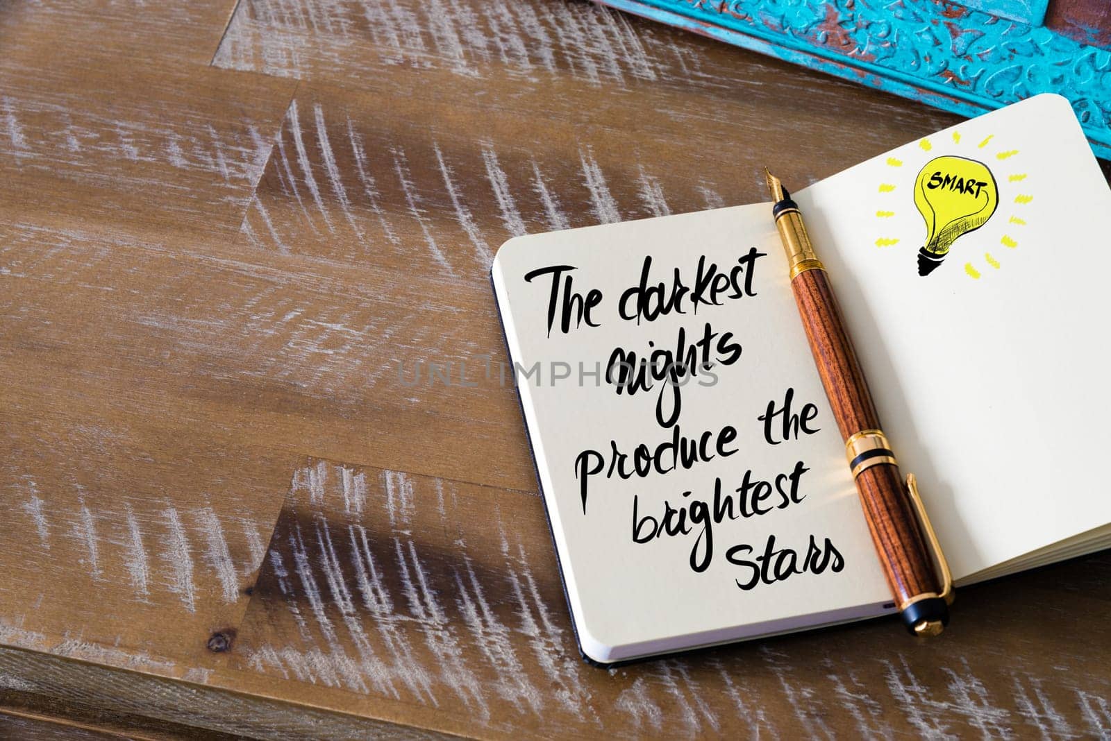 Handwritten text The darkest nights produce the brightest stars with fountain pen on notebook. Concept image with copy space available.