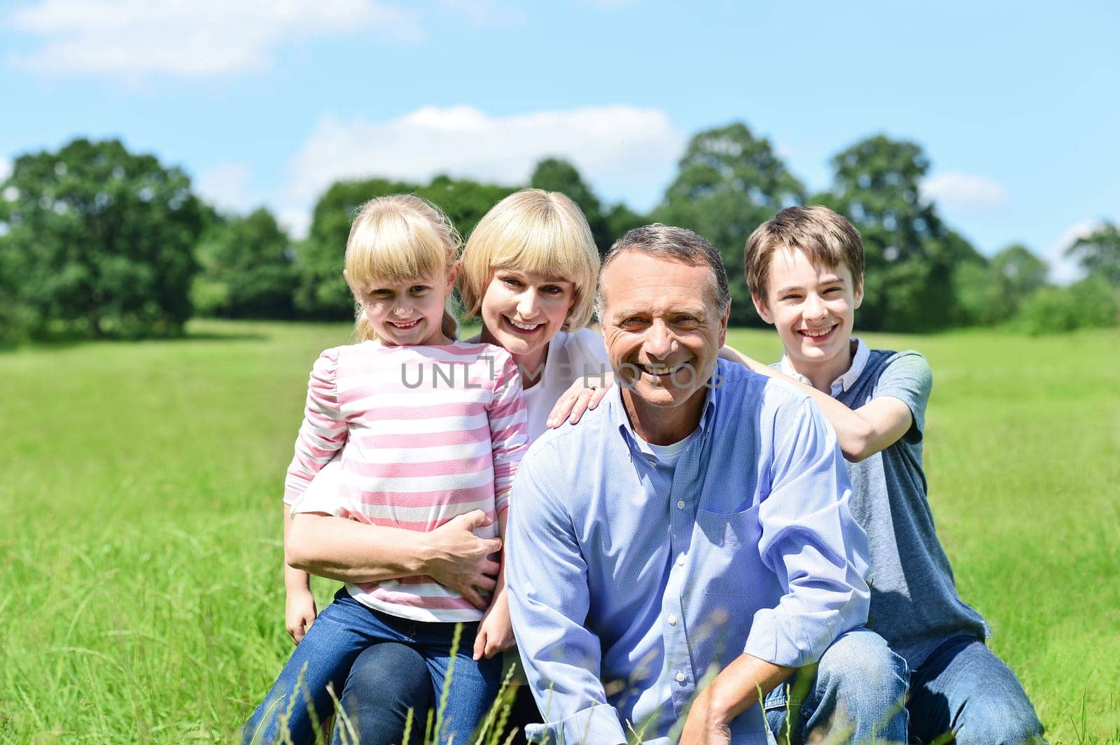 Photo of happy family of four sitting on grass.