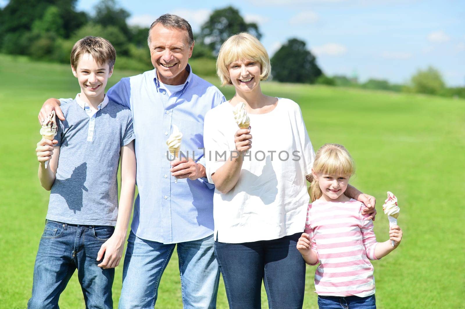 Family standing at grassfield with ice cream and smiling