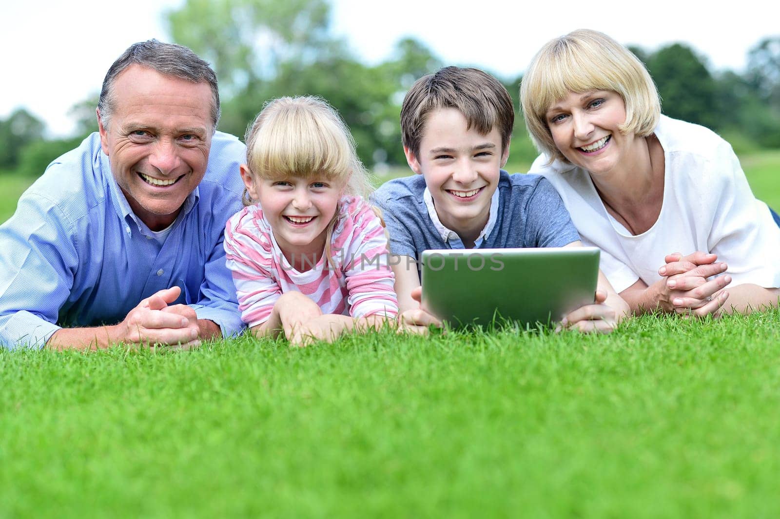 Happy family of four lying in summer park with tablet PC