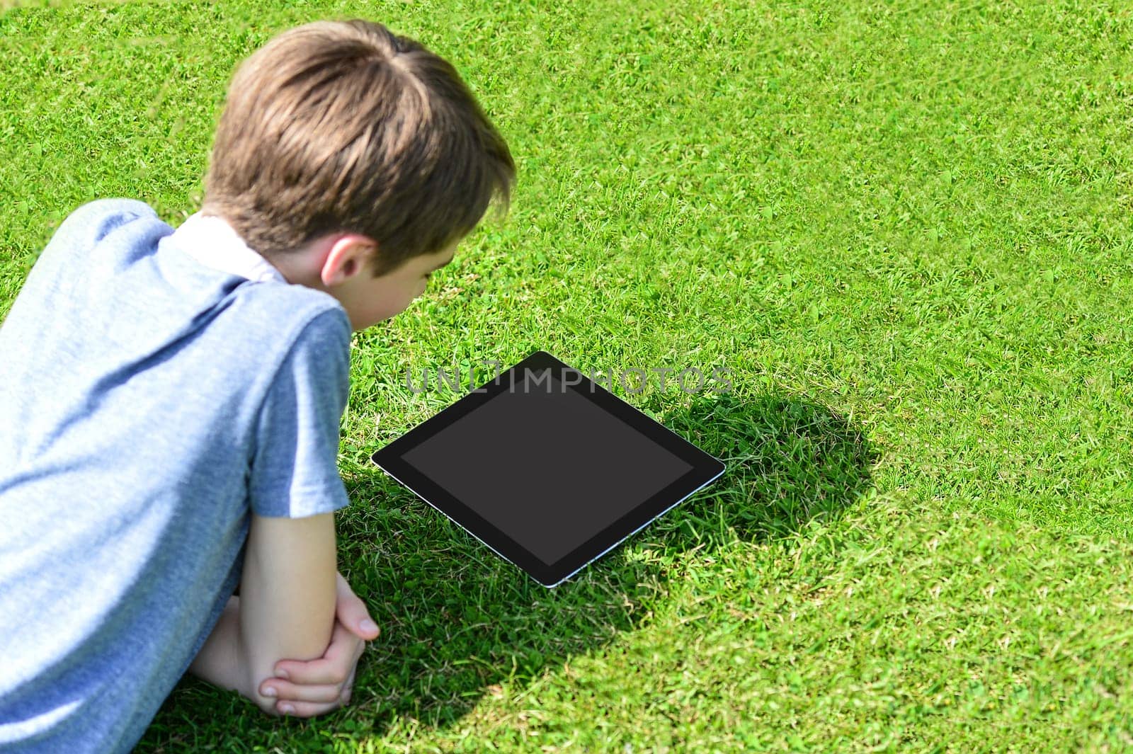Cute boy lying on grass in park and using tablet pc