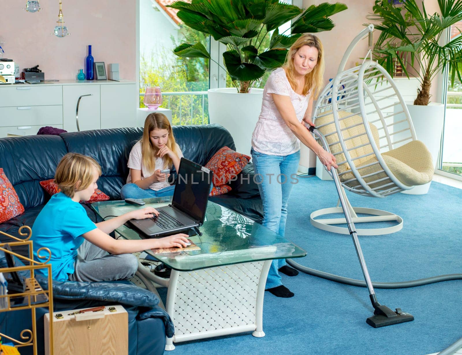 boy playing with computer, his sister using smartphone at home and mother doing homework