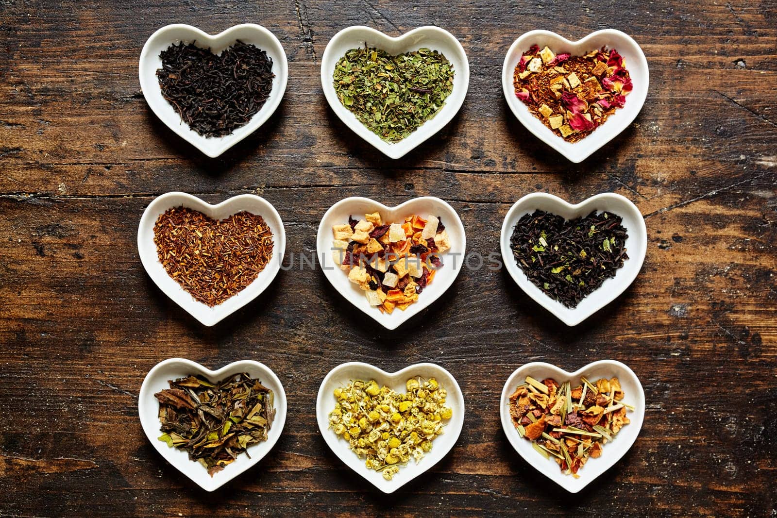 Set of nine assorted sorts of raw tea in tiny bowls shaped as hearts on weathered wooden surface