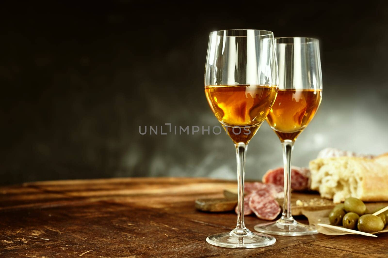 Two glasses of sherry served with tasty traditional Spanish tapas of olives, salami and fresh bread on an old wooden table with copy space