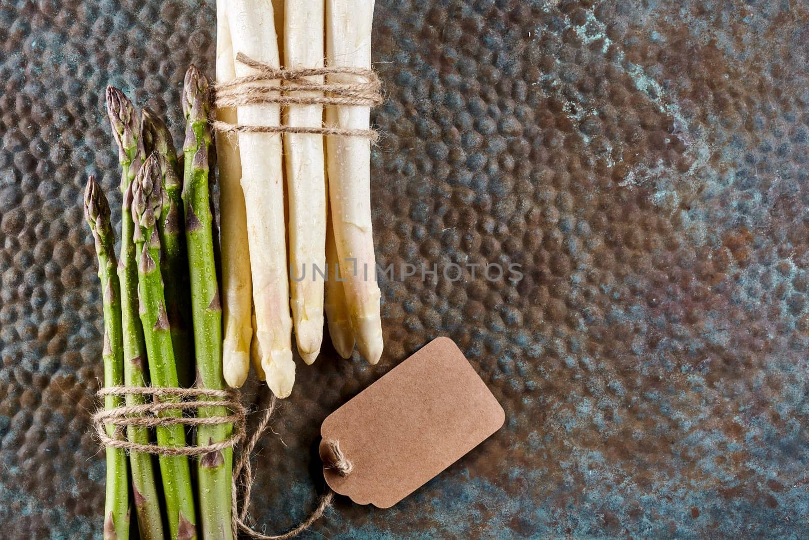 High Angle Still Life View of White and Green Asparagus Stalks Bound Together with Twine and Blank Tag, Lying Side by Side on Textured Rusty Metal Surface with Copy Space