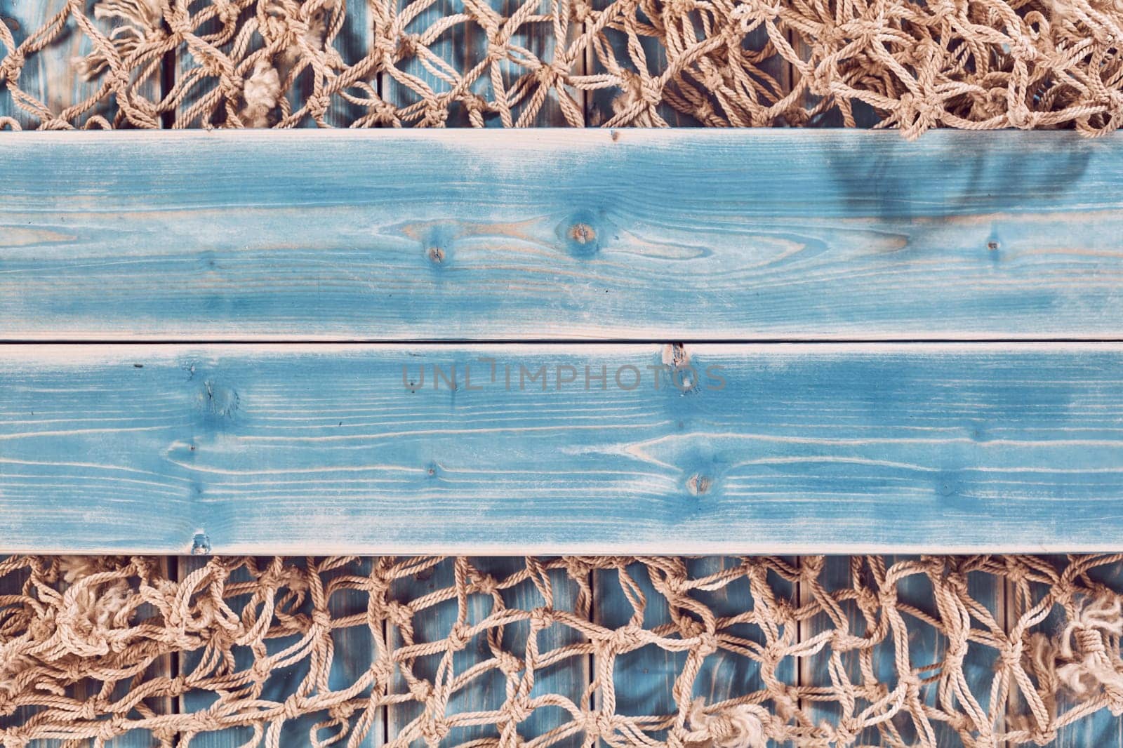 High Angle Still Life of Planks of Blue Painted Wood Horizontal Through Center of Frame and Overlay on Natural Rope Fishing Net - Nautical Themed Background with Copy Space