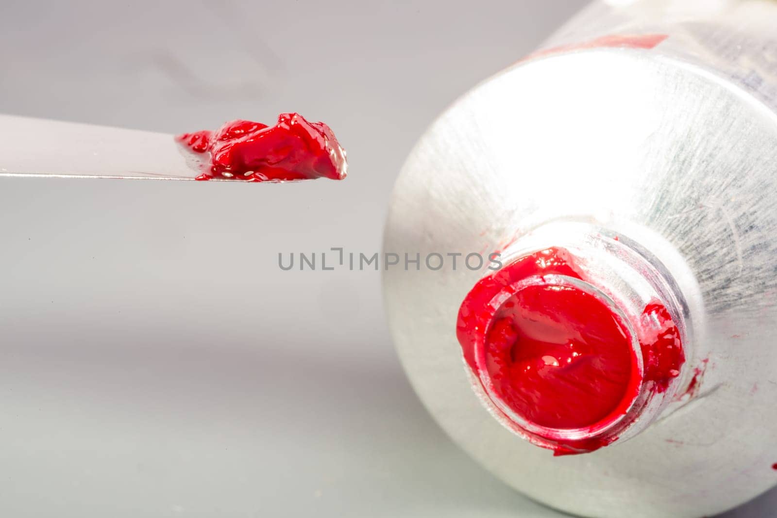 A small amount of red oil paint is taken with the tip of a paint knife from the tube of the paint.