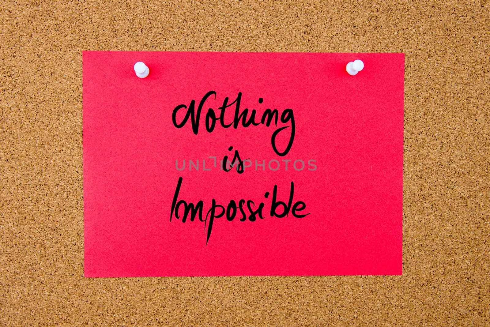 Red paper note with handwritten text Nothing Is Impossible pinned on cork board with white thumbtacks