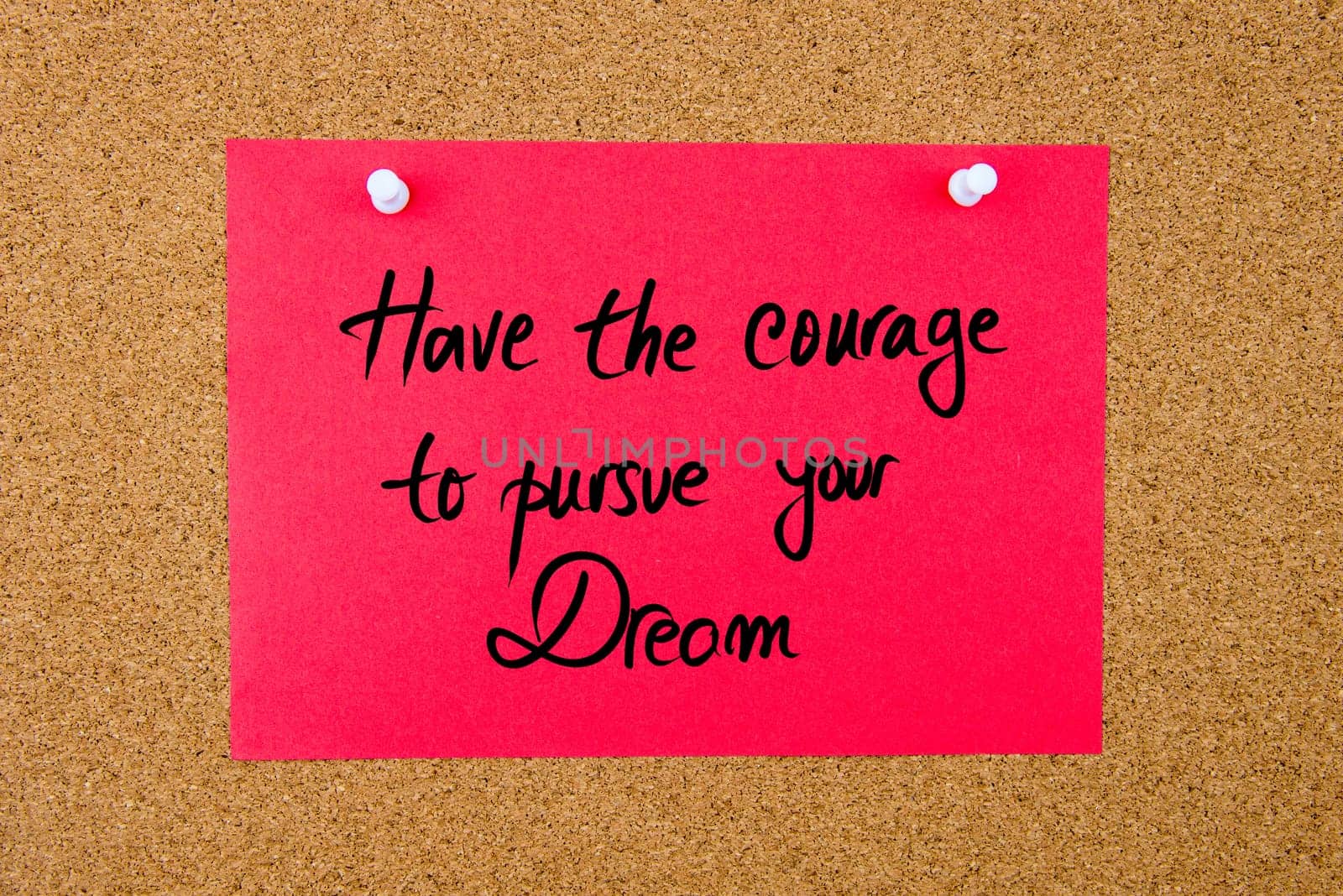 Red paper note with handwritten text Have The Courage To Pursue Your Dream pinned on cork board with white thumbtacks