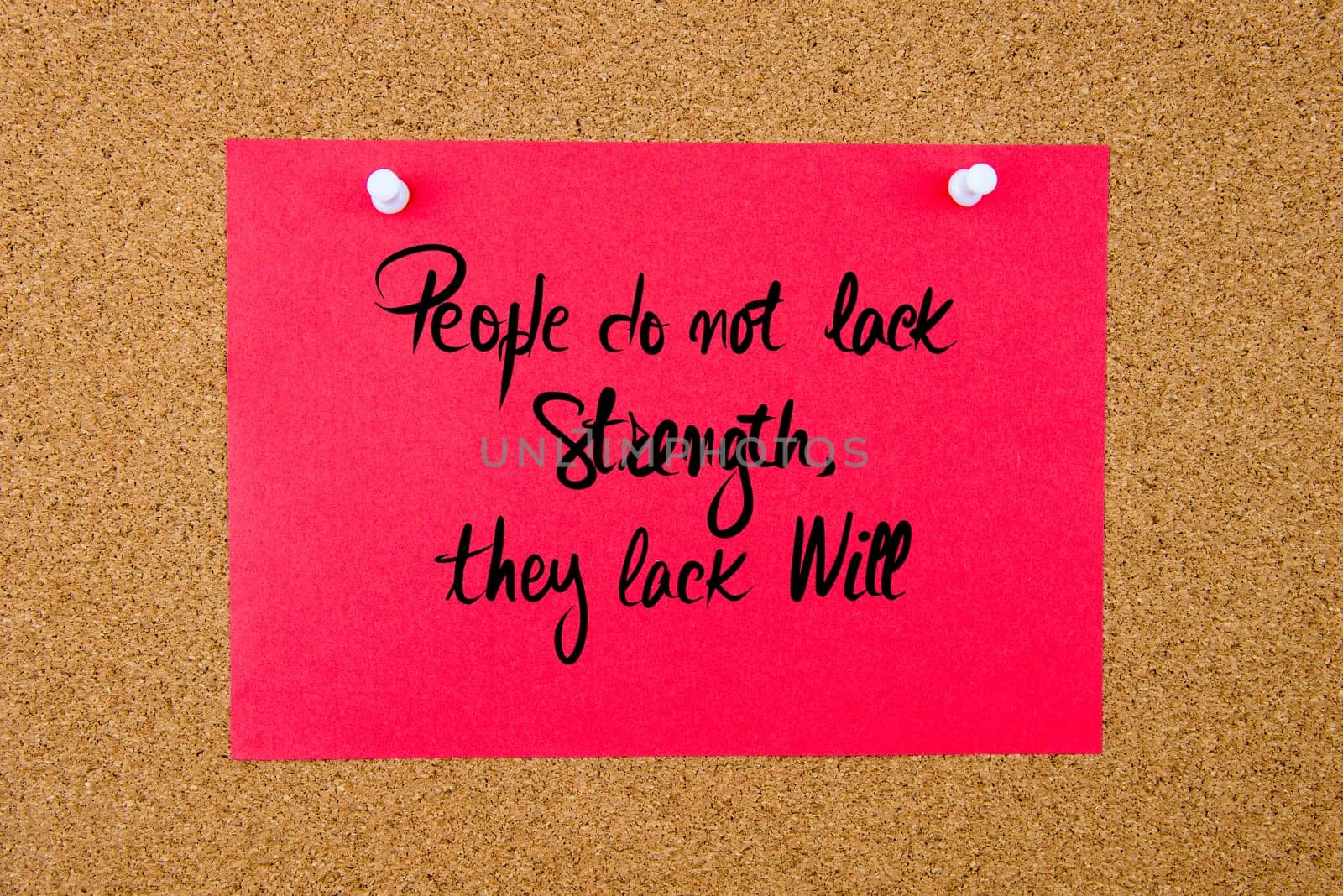 Red paper note with handwritten text People Do Not Lack Strength, They Lack Will pinned on cork board with white thumbtacks