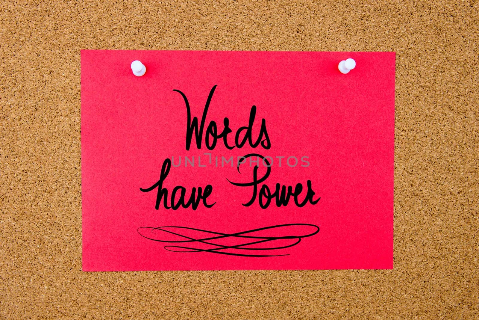 Red paper note with handwritten text Words Have Power pinned on cork board with white thumbtacks