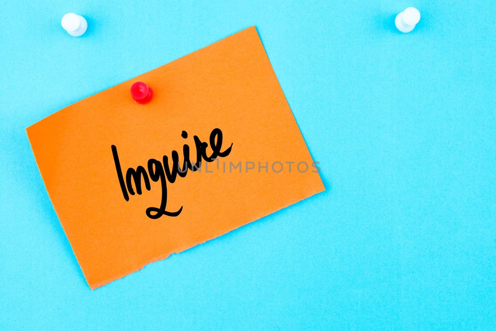 Inquire written on orange paper note pinned on cork board with white thumbtack, copy space available