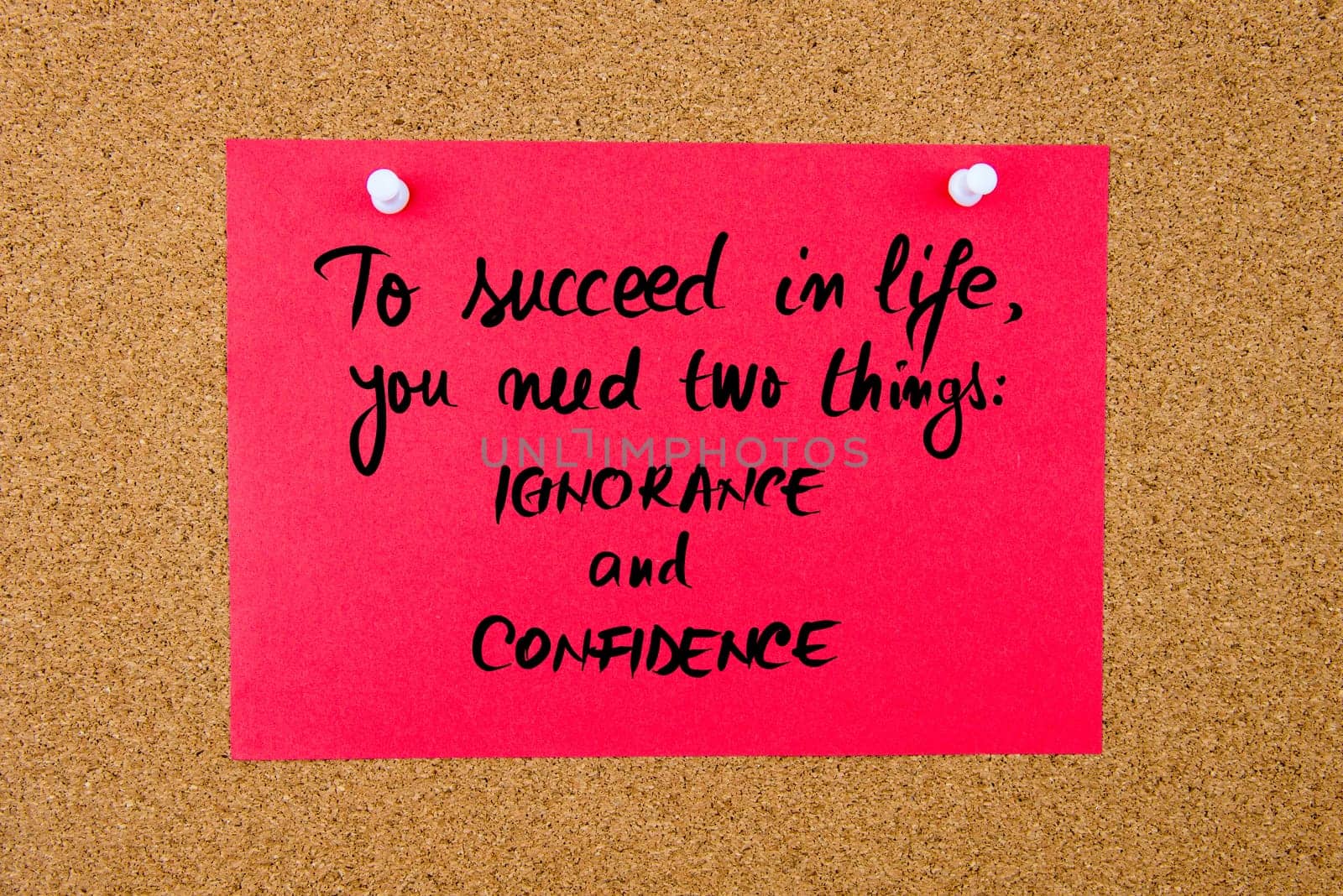 Red paper note with handwritten text To Succeed In Life You Need Two Things IGNORANCE and CONFIDENCE pinned on cork board with white thumbtacks