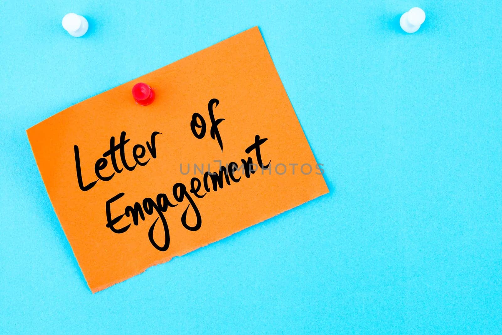 Letter Of Engagement written on orange paper note pinned on cork board with white thumbtack, copy space available