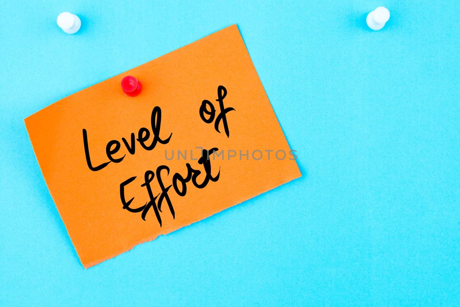 Level Of Effort written on orange paper note pinned on cork board with white thumbtack, copy space available