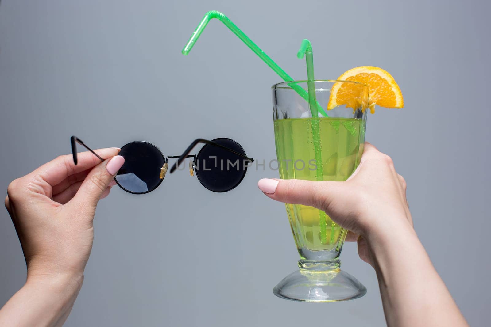 The female hands with cocktail and sunglasses on a gray background