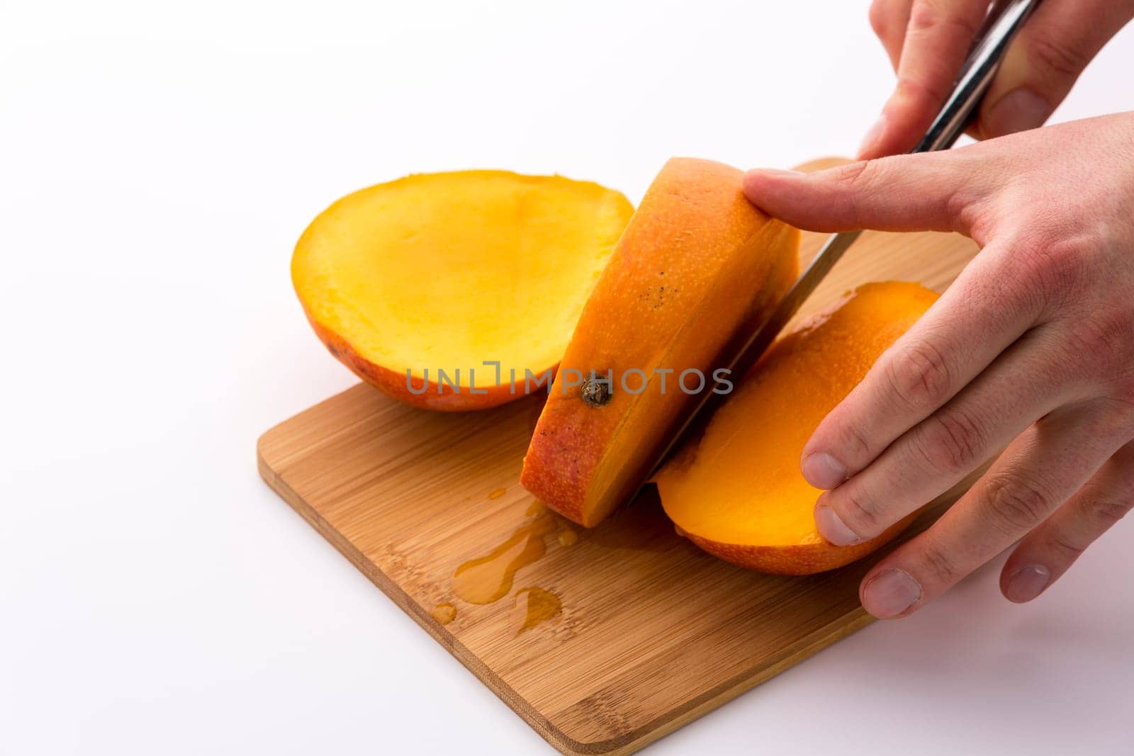 Knife finishing a second cut through a ripe mango. Forcing apart a third slice from the middle slab containing the fruit pip does reveal tangerine, juicy pulp of this tropical delicacy. White ground.