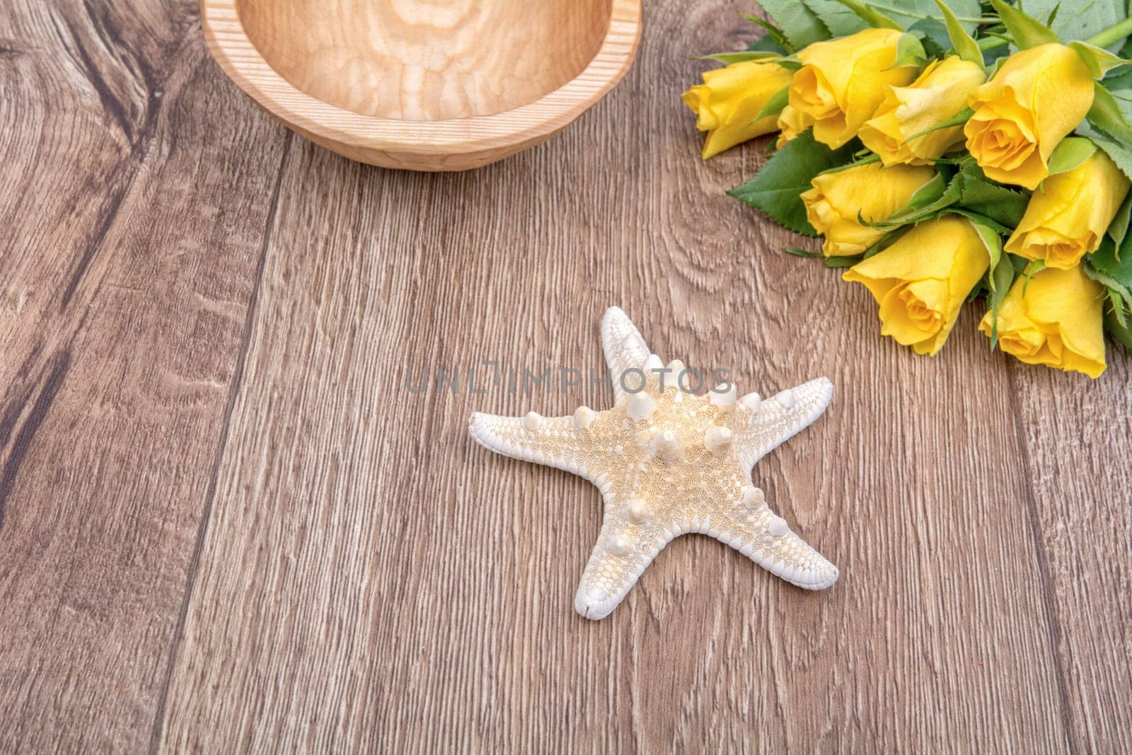 White starfish and yellow roses on a wooden background