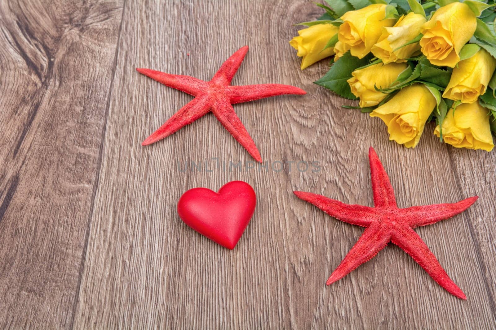 Red starfishes, heart and yellow roses on a wooden background