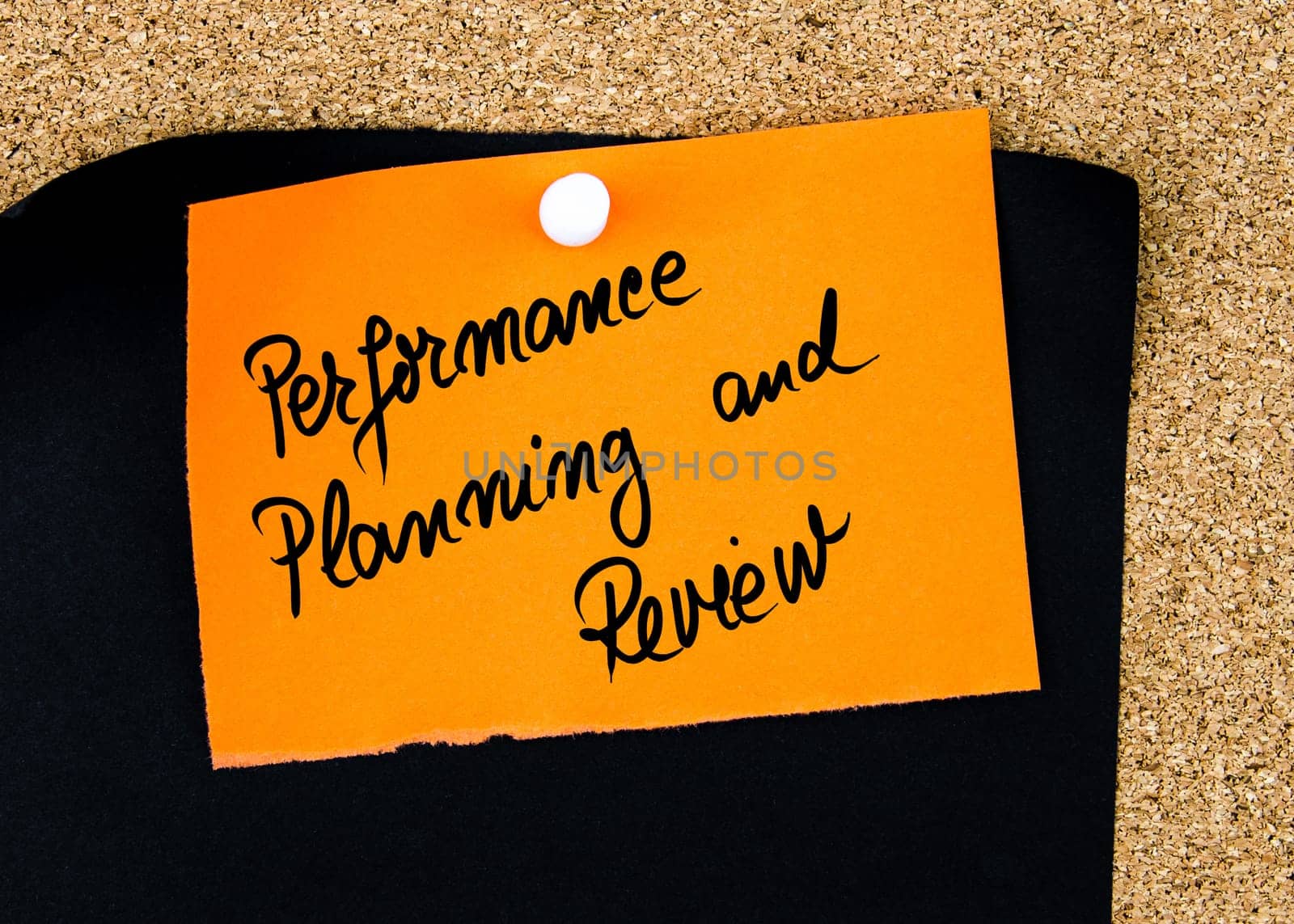 Performance Planning and Review written on orange paper note pinned on cork board with white thumbtacks, copy space available