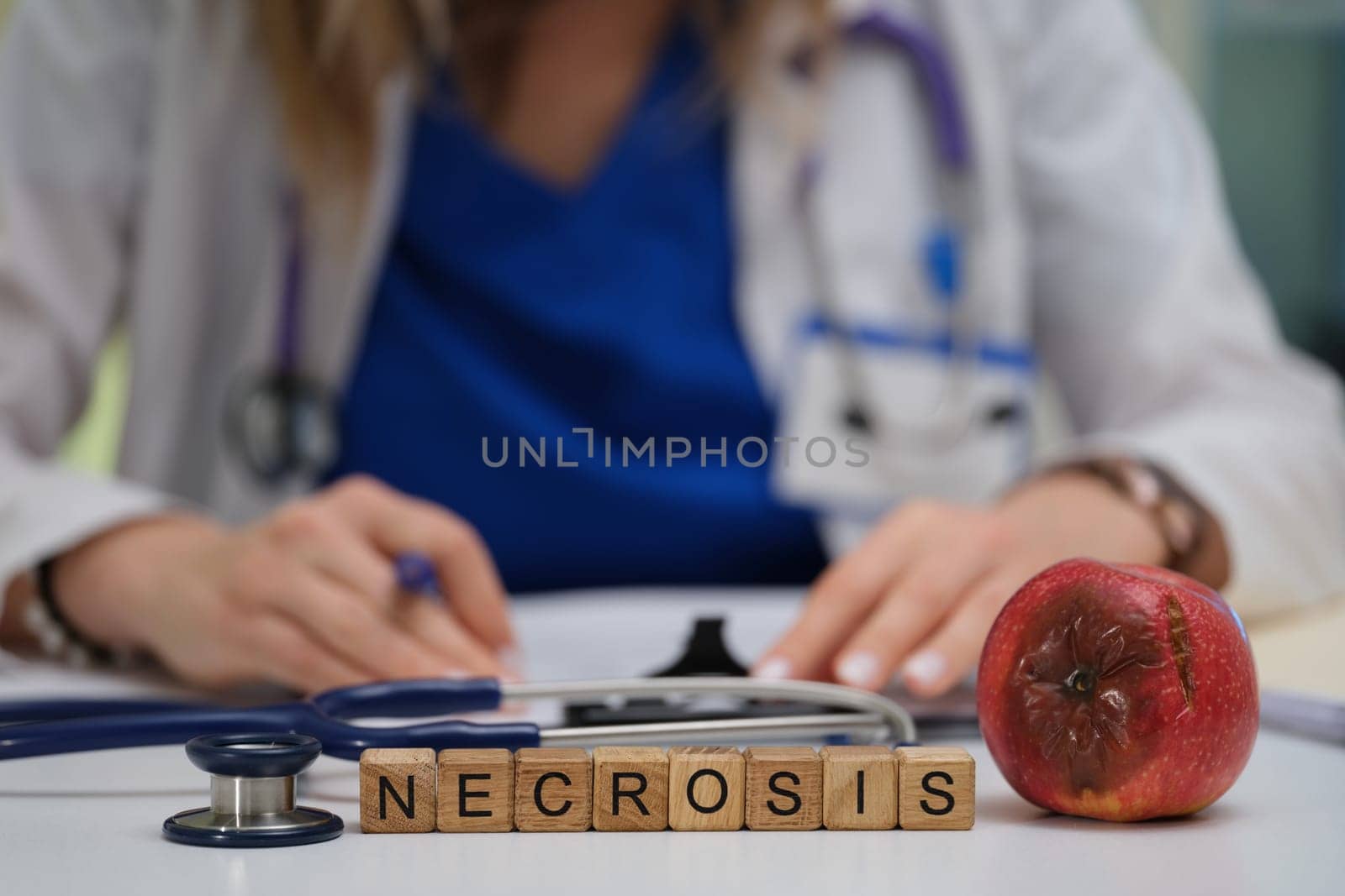 A medical professional conducts an examination of necrosis, symbolically represented by an apple and wooden letters