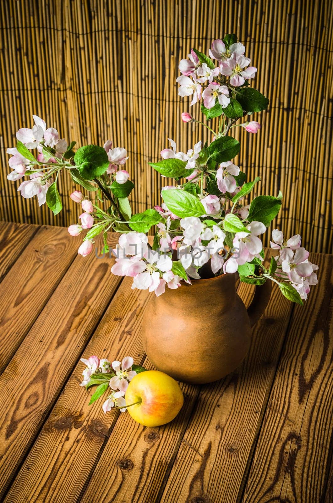Ripe apple and blossoming branch of an apple-tree in a clay jar, close-up