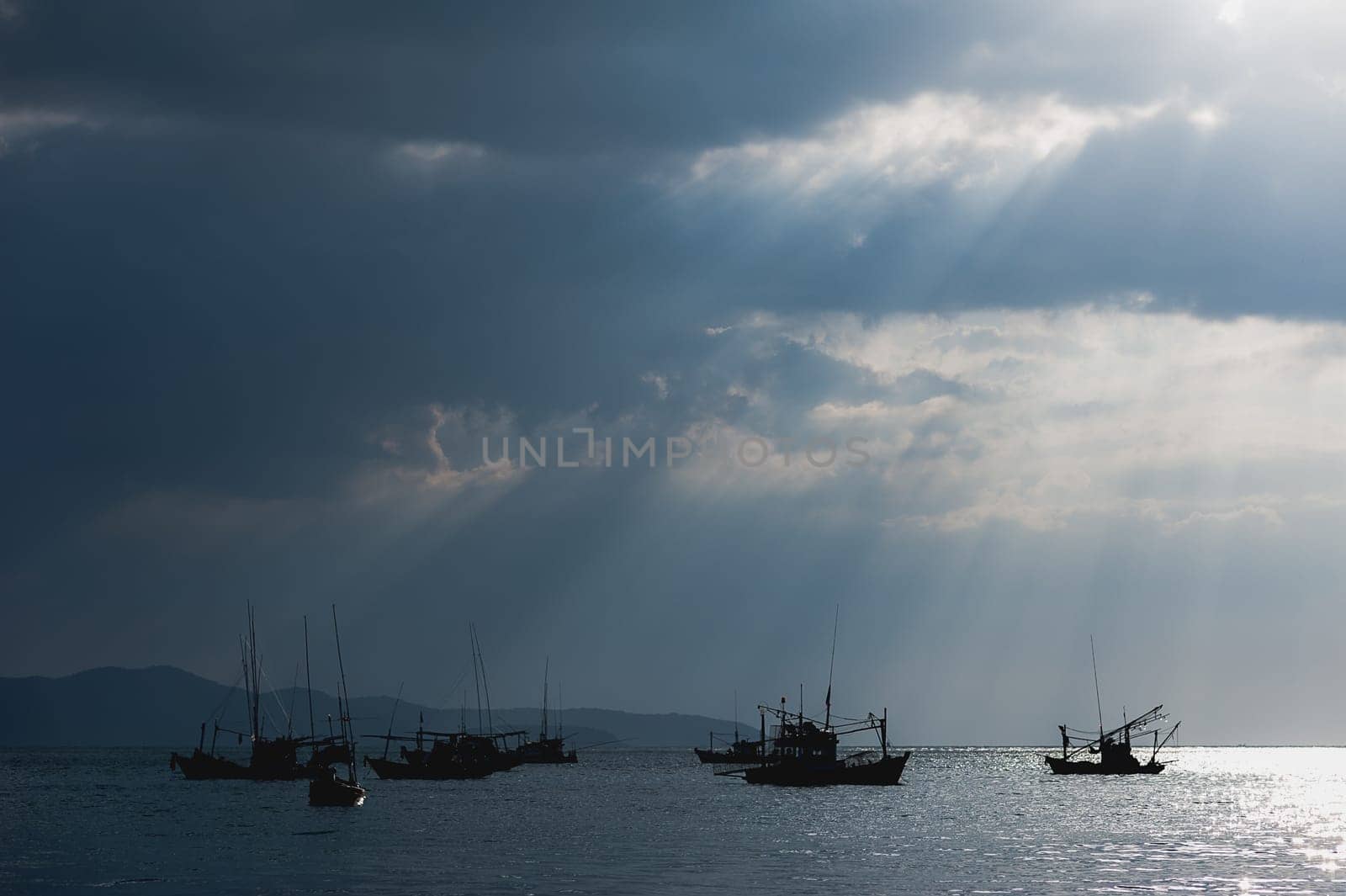 Scenery of fishing boats and yachts with sunlight shining through cloudy sky and reflections of golden clouds on smooth water, in Thailand