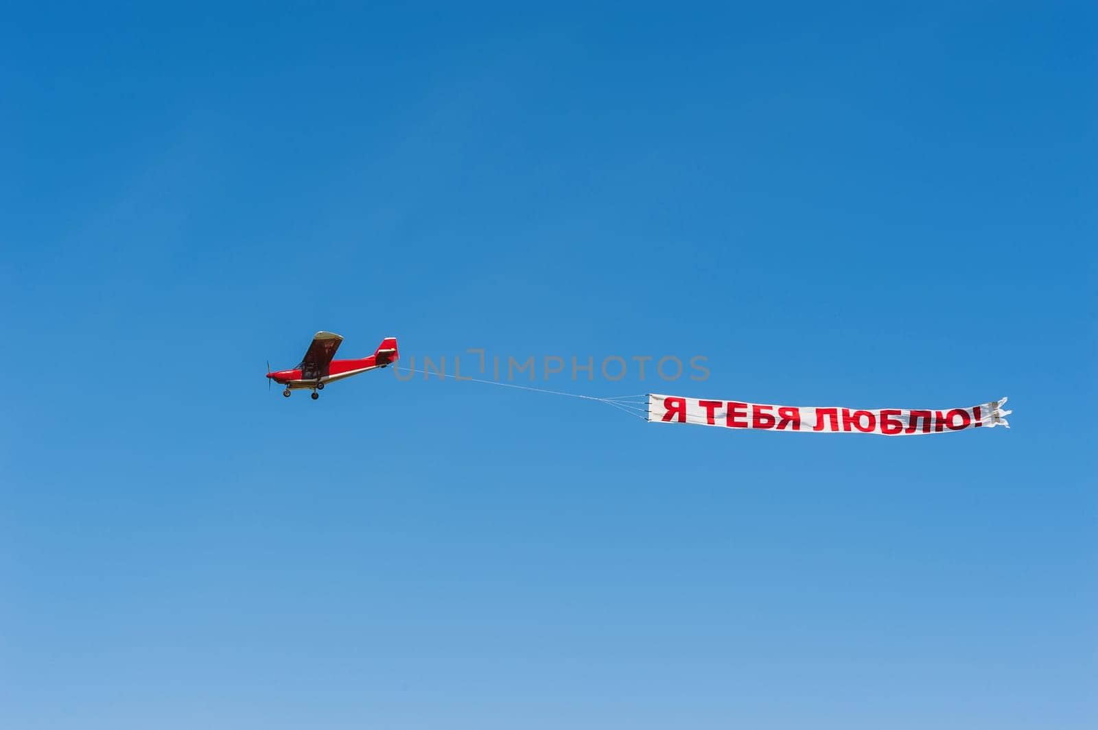 red propeller plane in a blue sky with a banner I love you, at the air show in Pervushin, Ufa, Bashkortostan on May 9, 2016