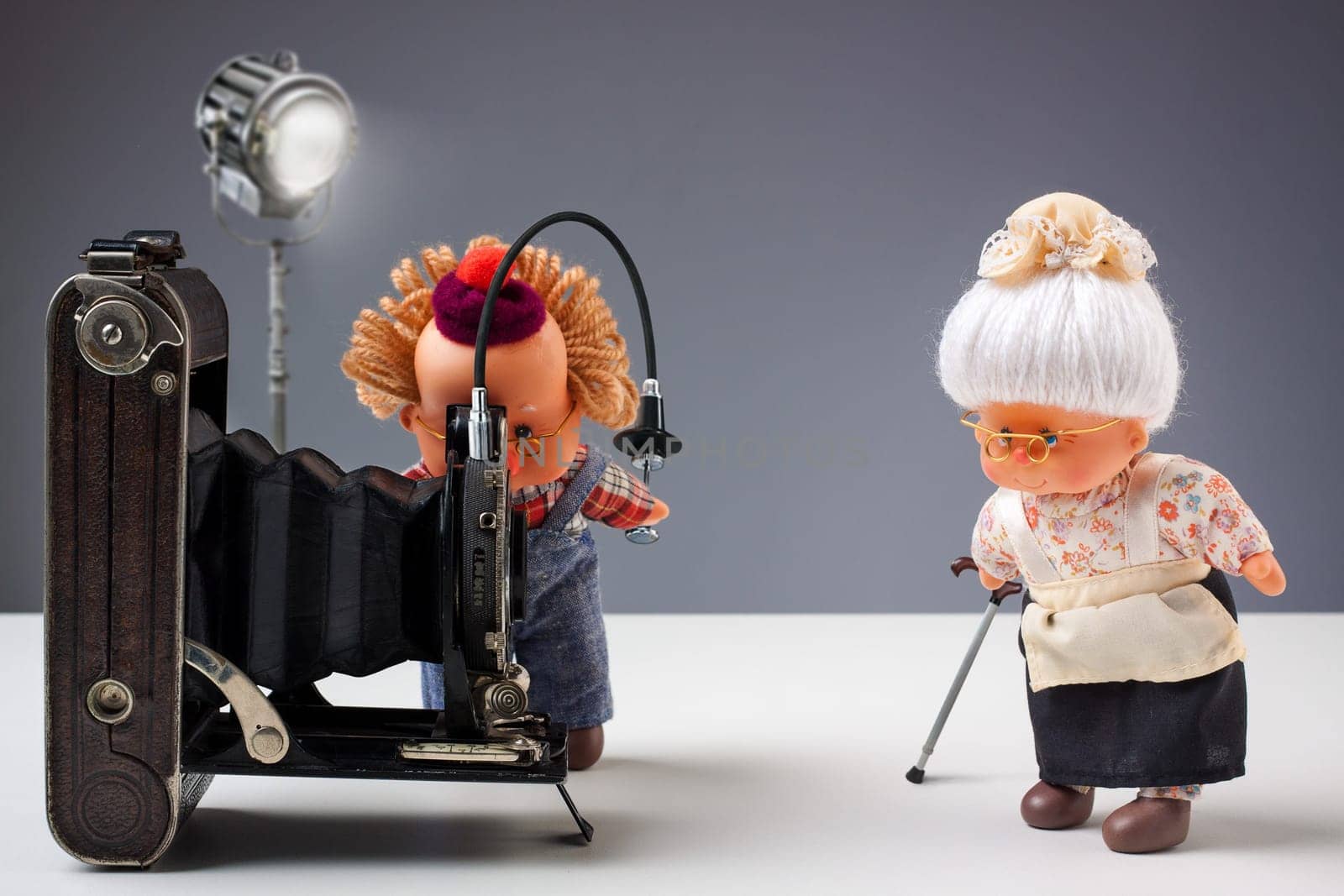 Puppets of senior photographer taking pictures of his old ladies with vintage camera in studio