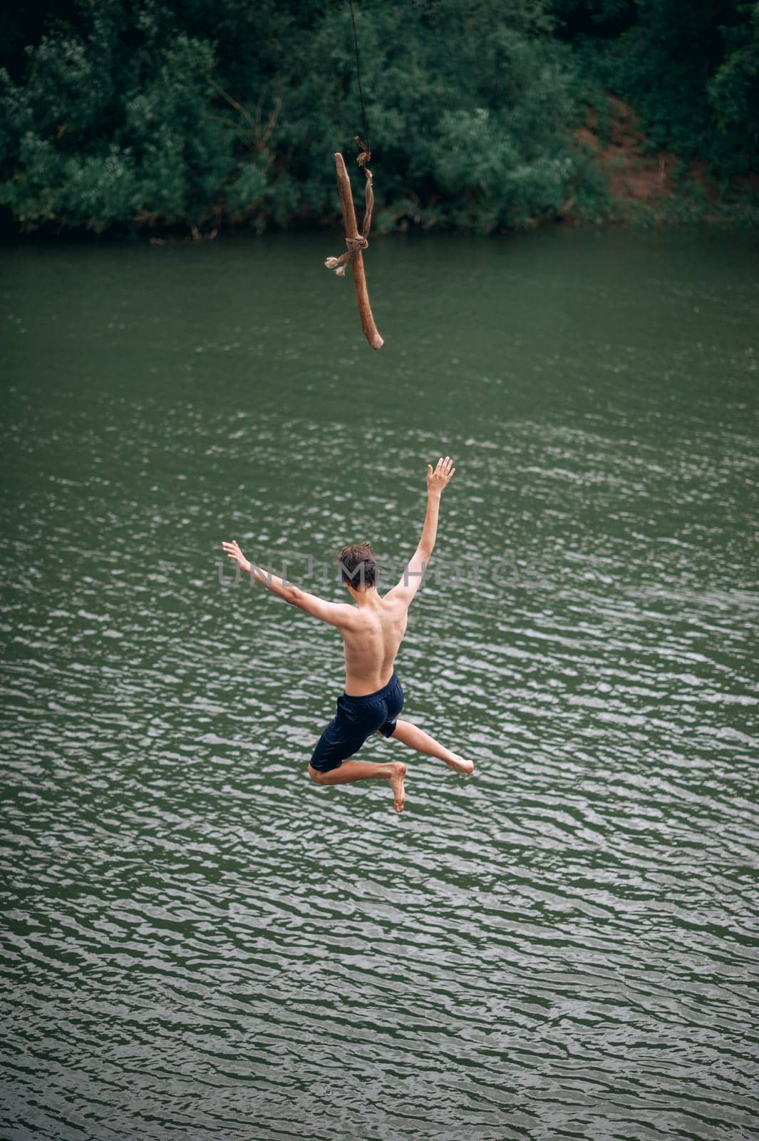 a young man jumping with a rope into the river, outdoors